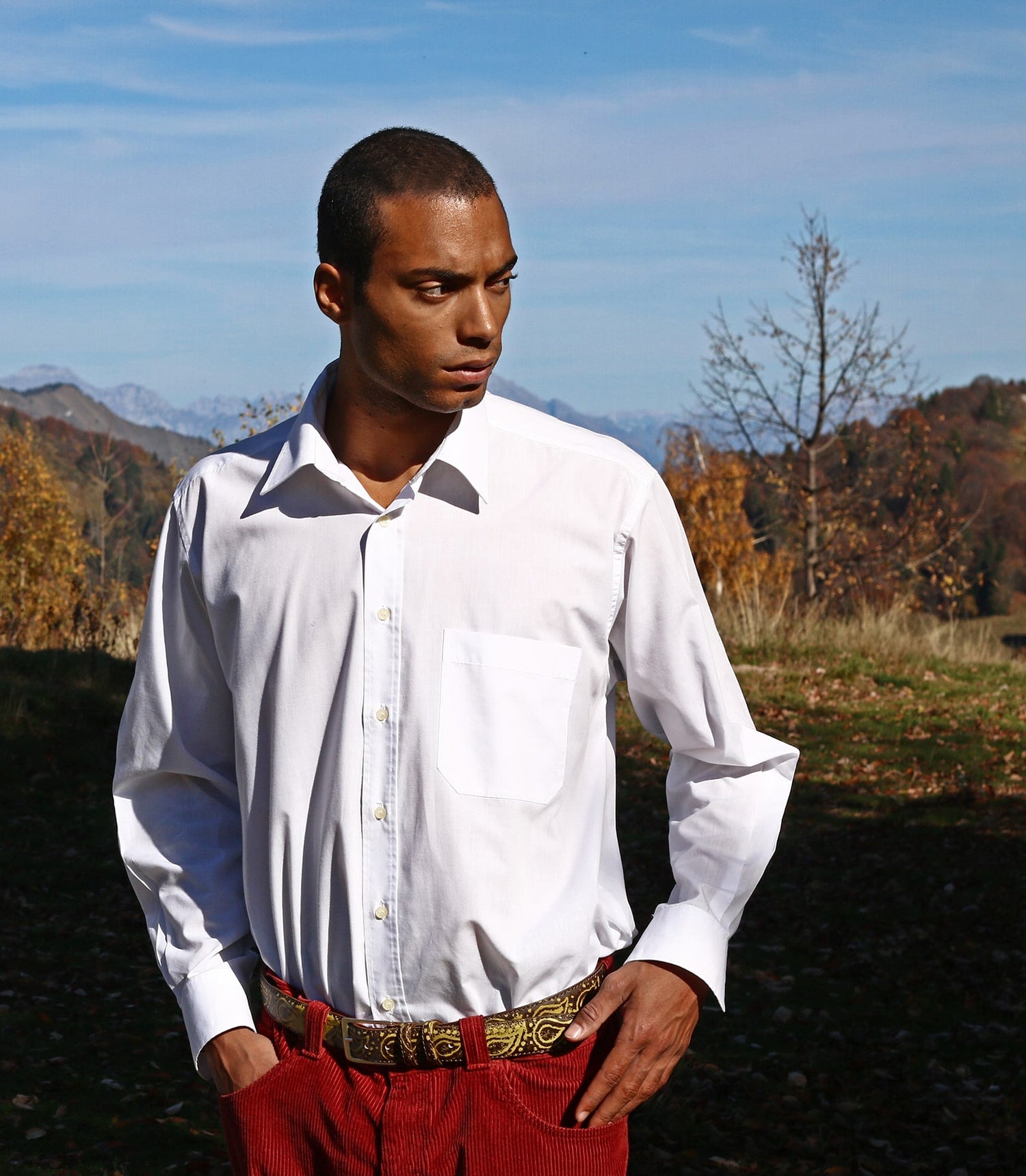 paisely painted belt weared by a guy with red trousers and white shirt, mountains on the background